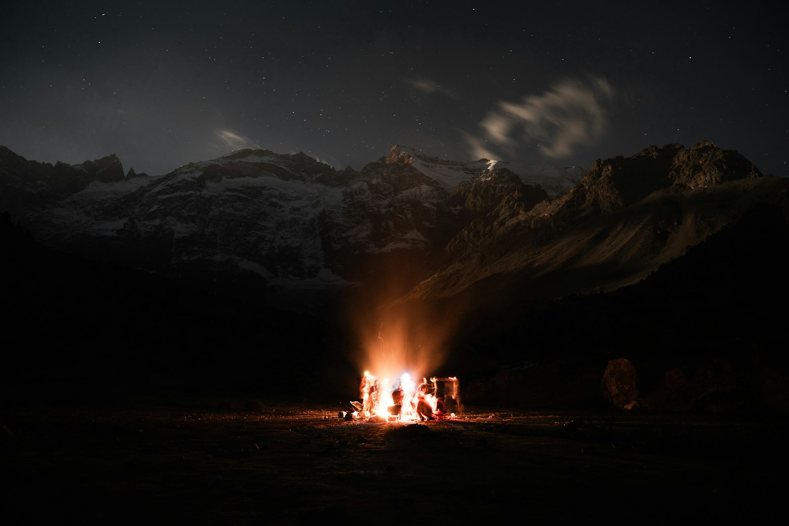 Campfire burning under a mountain night sky