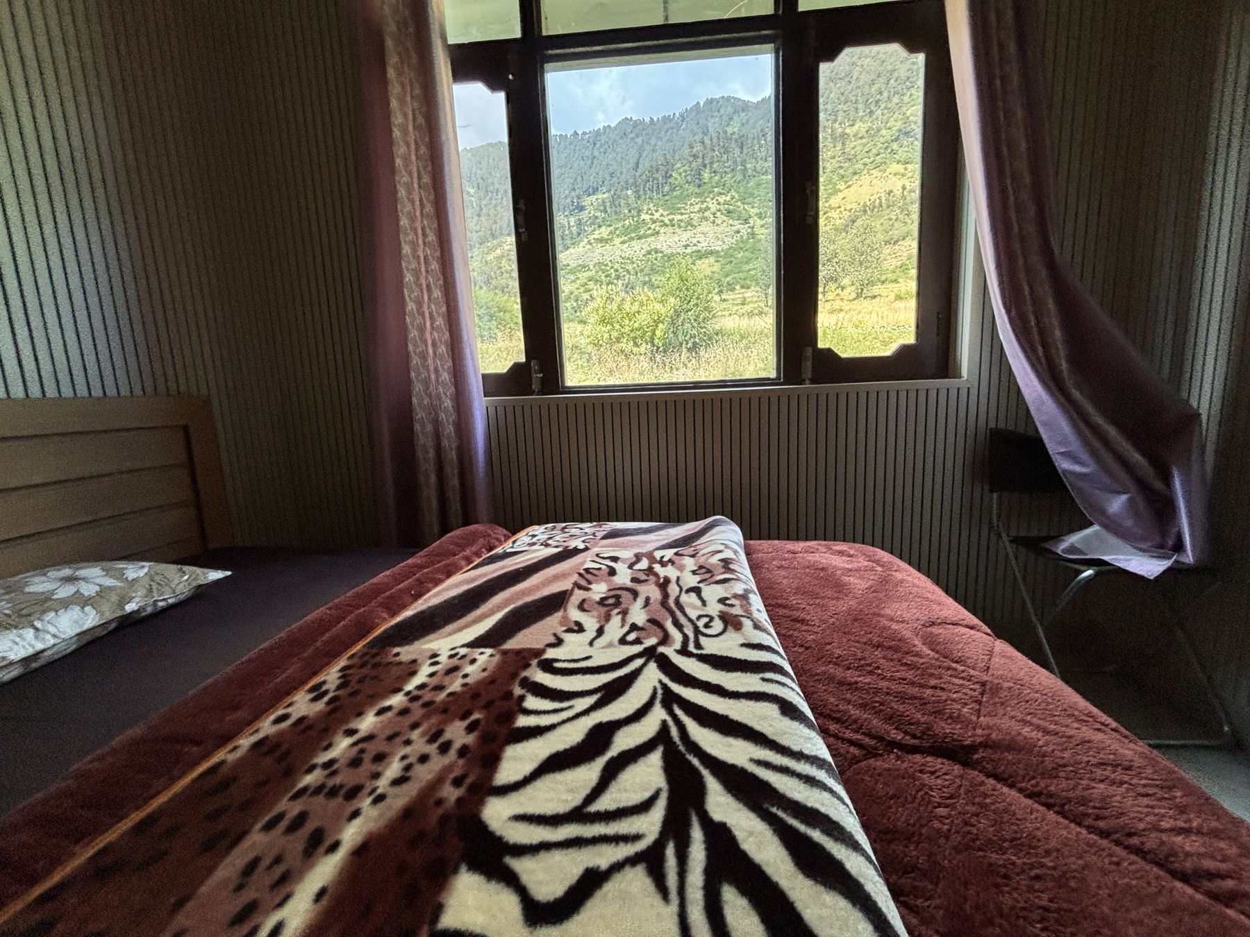 Bed turned down beside a window full of green hillside